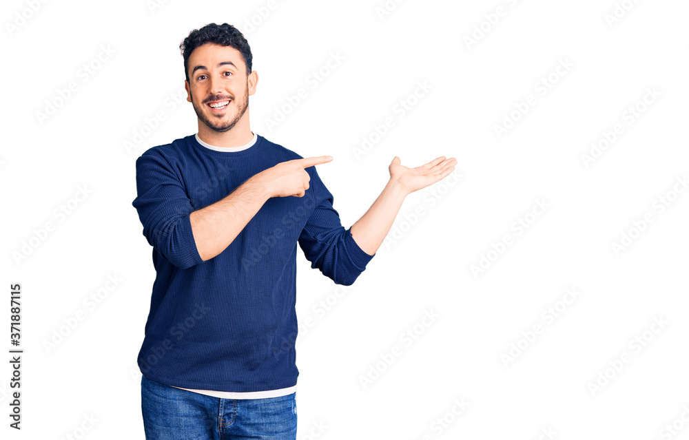 Young hispanic man wearing casual clothes amazed and smiling to the camera while presenting with hand and pointing with finger. Young hispanic man wearing casual clothes amazed and smiling to the camera while presenting with hand and pointing with finger.