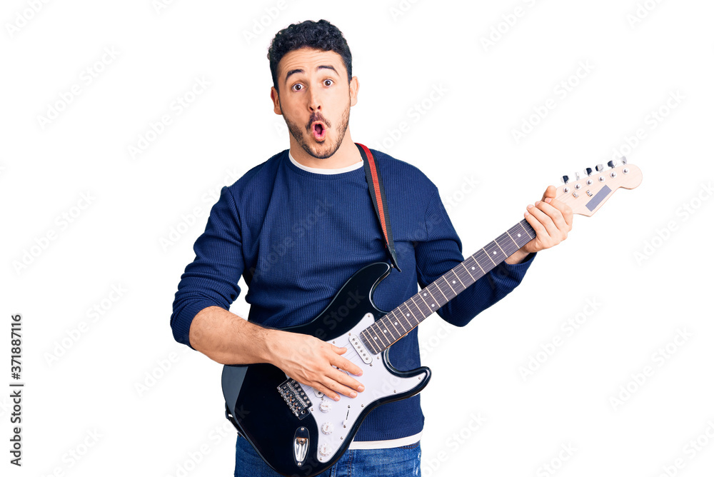 Young hispanic man playing electric guitar scared and amazed with open mouth for surprise, disbelief face Young hispanic man playing electric guitar scared and amazed with open mouth for surprise, disbelief face