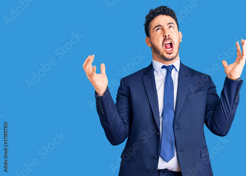 Young hispanic man wearing business clothes crazy and mad shouting and yelling with aggressive expression and arms raised. frustration concept.
