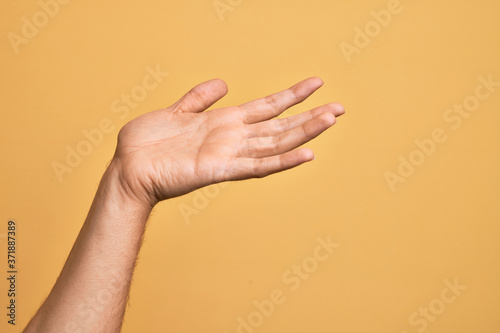 Hand of caucasian young man showing fingers over isolated yellow background presenting with open palm  reaching for support and help  assistance gesture