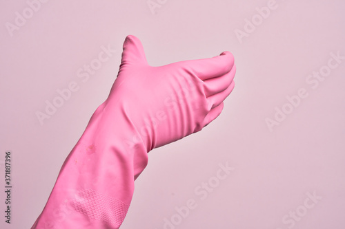 Hand of caucasian young man with cleaning glove over isolated pink background holding invisible object, empty hand doing clipping and grabbing gesture