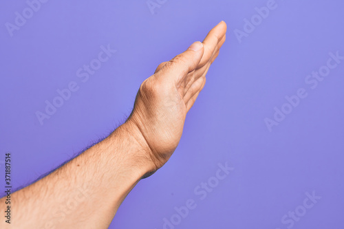 Hand of caucasian young man showing fingers over isolated purple background showing side of stretched hand, pushing and doing stop gesture