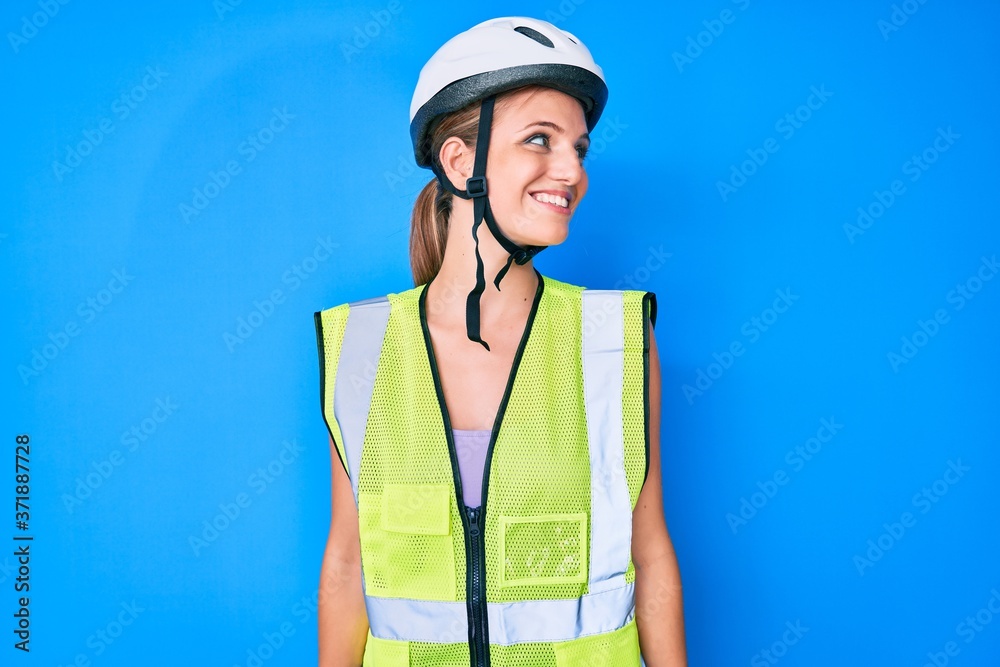Young caucasian girl wearing bike helmet and reflective vest looking away to side with smile on face, natural expression. laughing confident. Young caucasian girl wearing bike helmet and reflective vest looking away to side with smile on face, natural expression. laughing confident.
