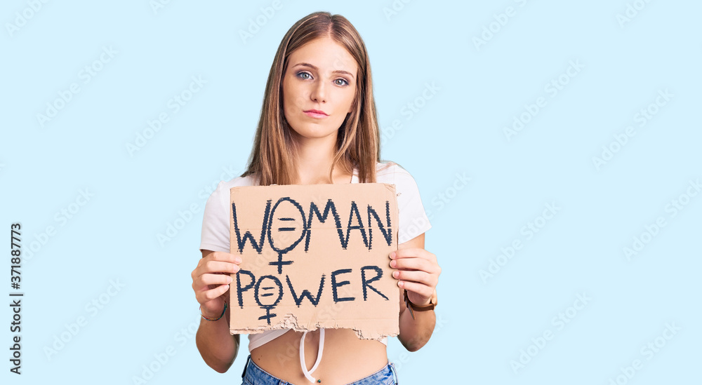 Young beautiful blonde woman holding woman power banner thinking attitude and sober expression looking self confident Young beautiful blonde woman holding woman power banner thinking attitude and sober expression looking self confident