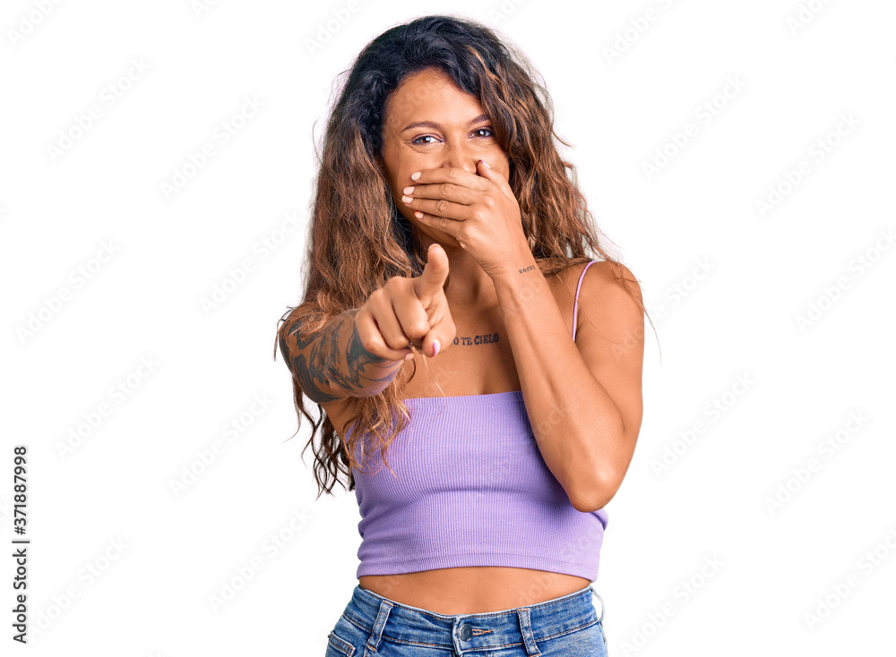 Young hispanic woman with tattoo wearing casual clothes laughing at you, pointing finger to the camera with hand over mouth, shame expression