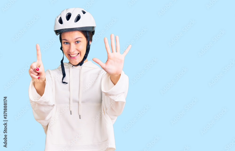 Beautiful brunette young woman wearing bike helmet and sporty clothes showing and pointing up with fingers number six while smiling confident and happy. Beautiful brunette young woman wearing bike helmet and sporty clothes showing and pointing up with fingers number six while smiling confident and happy.