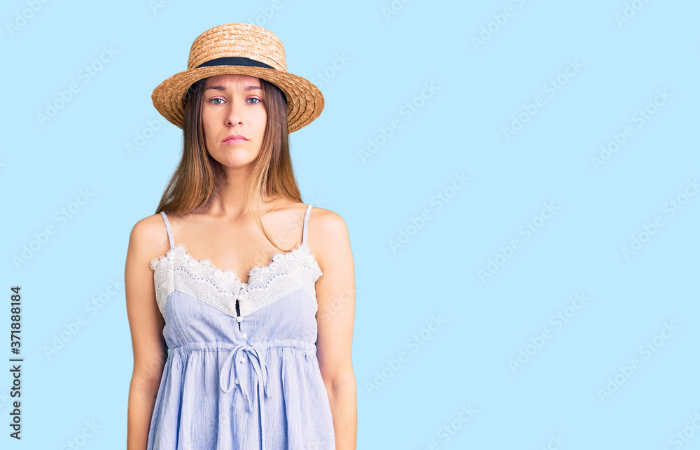 Beautiful brunette young woman wearing summer hat with serious expression on face. simple and natural looking at the camera.
