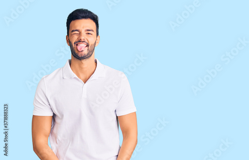 Young handsome hispanic man wearing casual clothes sticking tongue out happy with funny expression. emotion concept.