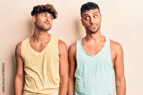 Young gay couple wearing casual clothes smiling looking to the side and staring away thinking.