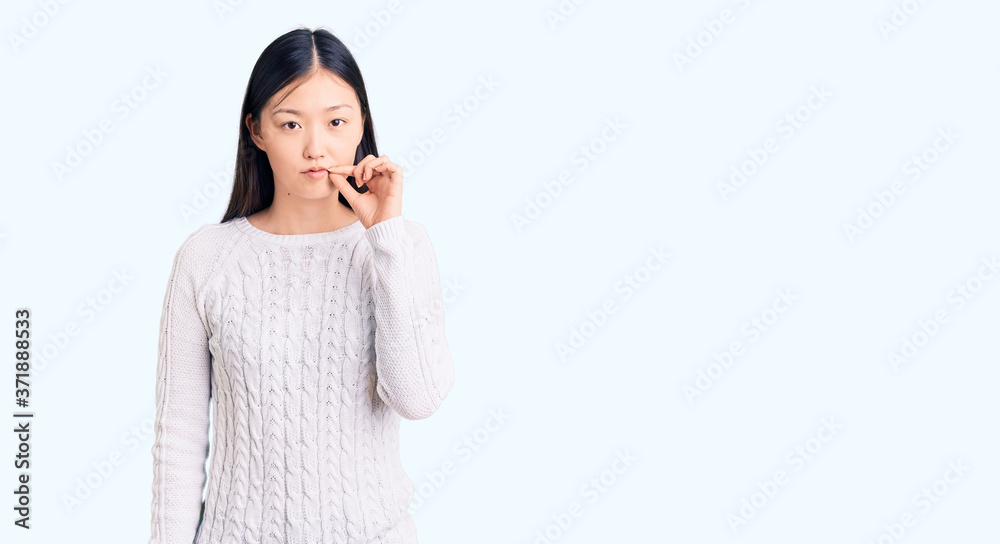 Young beautiful chinese woman wearing casual sweater mouth and lips shut as zip with fingers. secret and silent, taboo talking Young beautiful chinese woman wearing casual sweater mouth and lips shut as zip with fingers. secret and silent, taboo talking