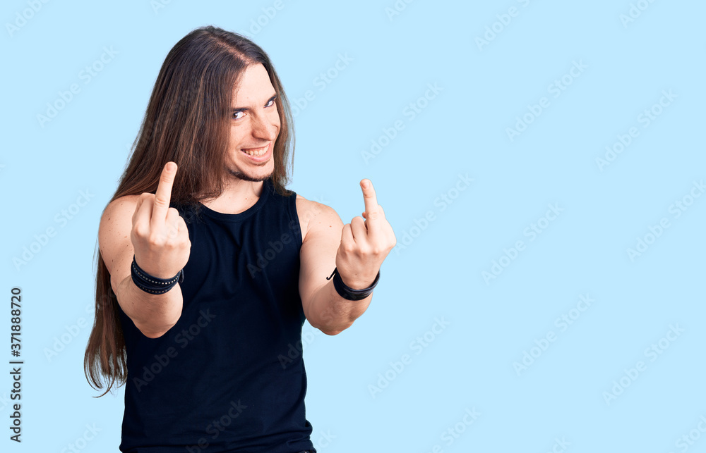 Young adult man with long hair wearing goth style with black clothes showing middle finger doing fuck you bad expression, provocation and rude attitude. screaming excited Young adult man with long hair wearing goth style with black clothes showing middle finger doing fuck you bad expression, provocation and rude attitude. screaming excited