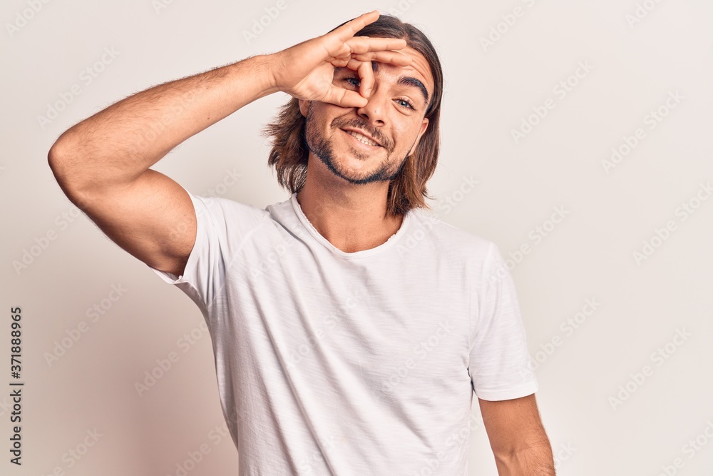 Young handsome man wearing casual clothes smiling happy doing ok sign with hand on eye looking through fingers Young handsome man wearing casual clothes smiling happy doing ok sign with hand on eye looking through fingers