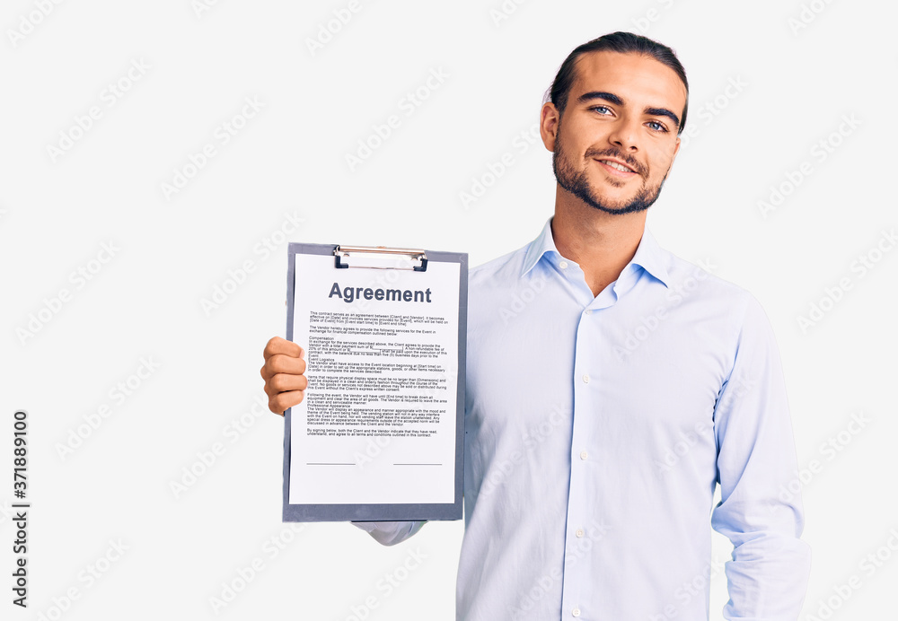 Young handsome man holding clipboard with agreement document looking positive and happy standing and smiling with a confident smile showing teeth Young handsome man holding clipboard with agreement document looking positive and happy standing and smiling with a confident smile showing teeth
