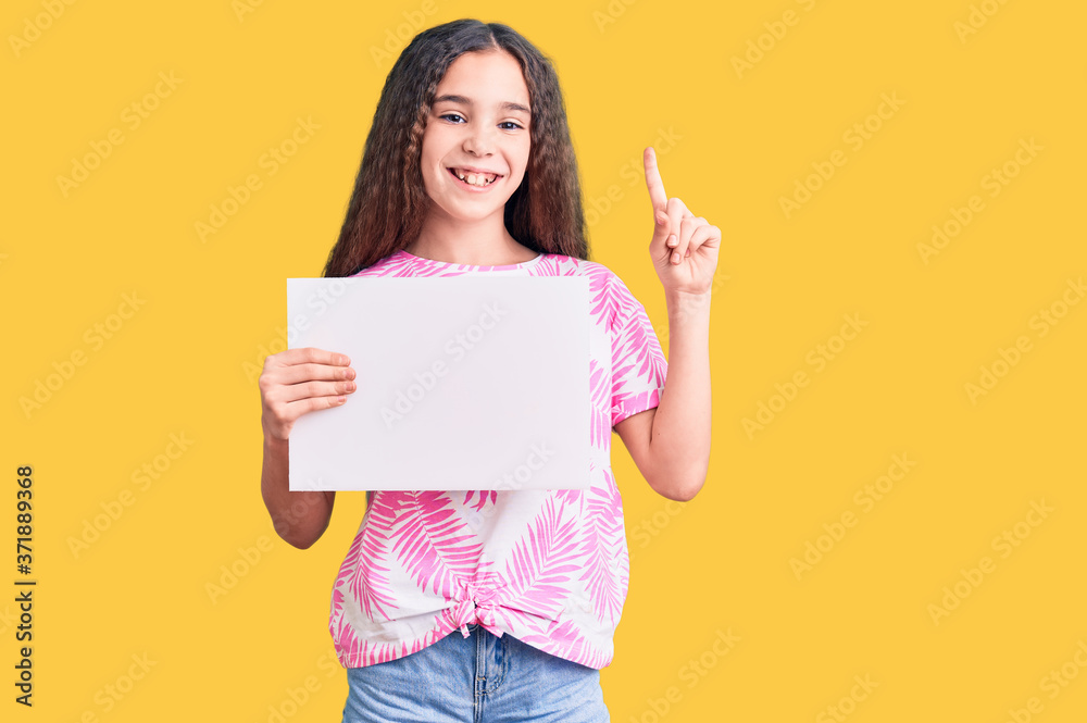 Cute hispanic child girl holding blank empty banner surprised with an idea or question pointing finger with happy face, number one Cute hispanic child girl holding blank empty banner surprised with an idea or question pointing finger with happy face, number one
