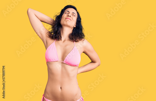 Young beautiful hispanic woman wearing bikini suffering of neck ache injury, touching neck with hand, muscular pain