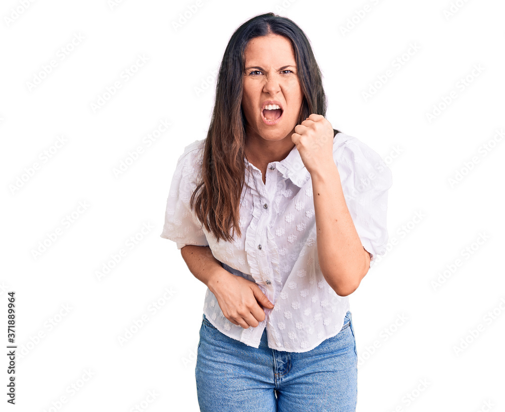 Young beautiful brunette woman wearing casual shirt angry and mad raising fist frustrated and furious while shouting with anger. rage and aggressive concept. Young beautiful brunette woman wearing casual shirt angry and mad raising fist frustrated and furious while shouting with anger. rage and aggressive concept.