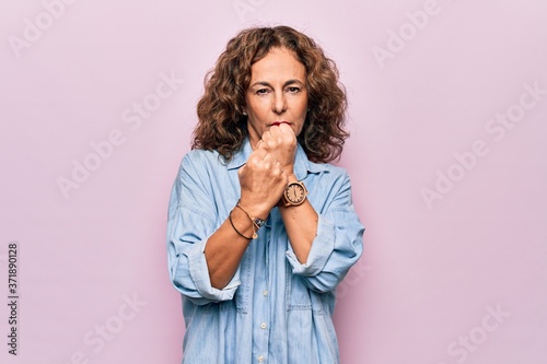 Middle age beautiful woman wearing casual denim shirt standing over pink background Ready to fight with fist defense gesture, angry and upset face, afraid of problem
