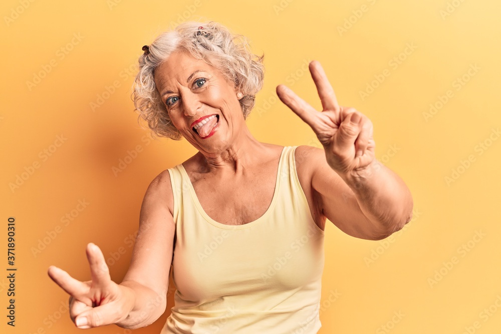 Senior grey-haired woman wearing casual clothes smiling with tongue out showing fingers of both hands doing victory sign. number two. Senior grey-haired woman wearing casual clothes smiling with tongue out showing fingers of both hands doing victory sign. number two.