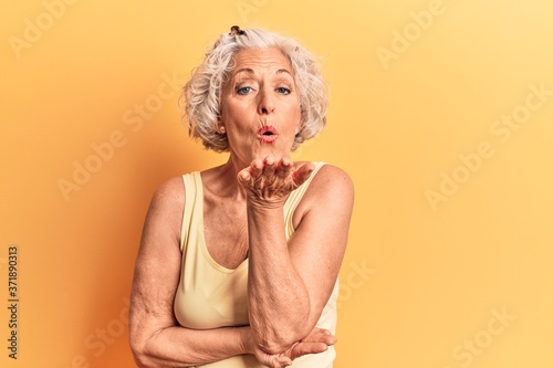 Senior grey-haired woman wearing casual clothes looking at the camera blowing a kiss with hand on air being lovely and sexy. love expression.