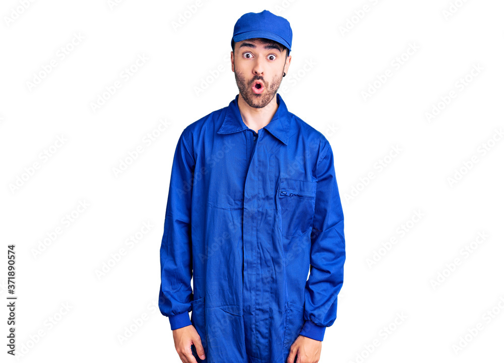 Young hispanic man wearing painter uniform scared and amazed with open mouth for surprise, disbelief face