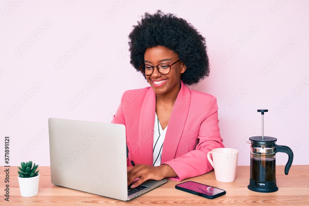Young african american woman working at desk using computer laptop looking positive and happy standing and smiling with a confident smile showing teeth Young african american woman working at desk using computer laptop looking positive and happy standing and smiling with a confident smile showing teeth