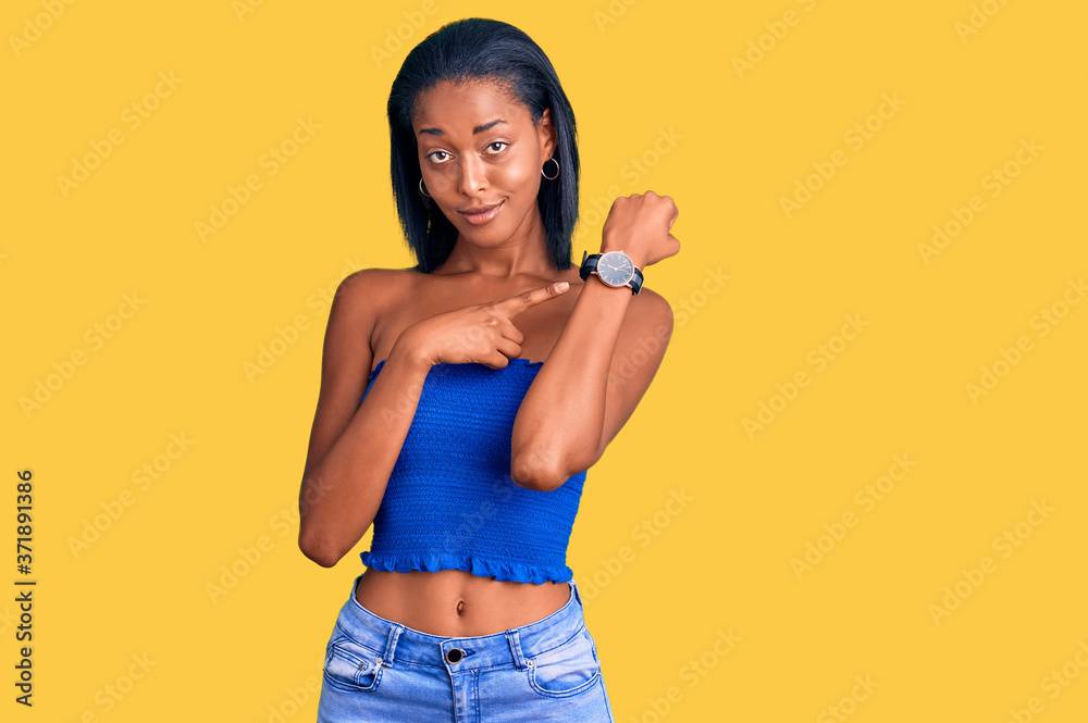 Young african american woman wearing casual summer clothes in hurry pointing to watch time, impatience, looking at the camera with relaxed expression Young african american woman wearing casual summer clothes in hurry pointing to watch time, impatience, looking at the camera with relaxed expression