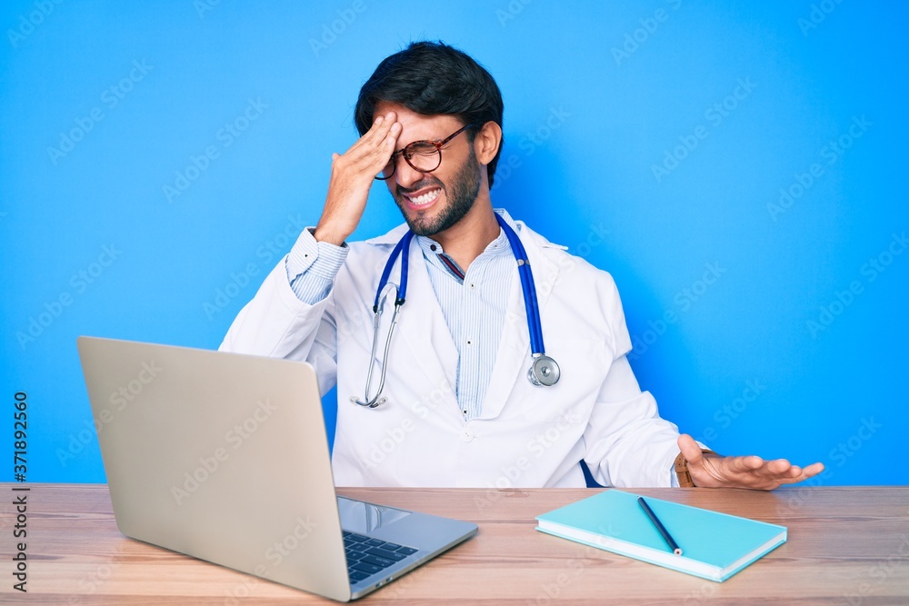 Handsome hispanic man wearing doctor uniform working at the clinic surprised with hand on head for mistake, remember error. forgot, bad memory concept. Handsome hispanic man wearing doctor uniform working at the clinic surprised with hand on head for mistake, remember error. forgot, bad memory concept.