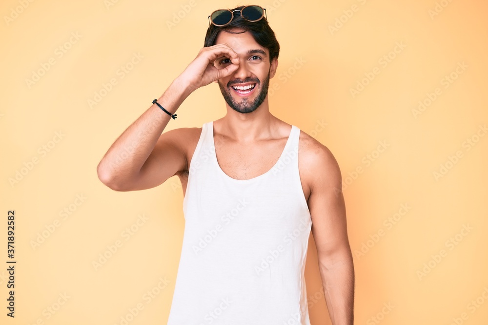 Handsome hispanic man wearing summer look and sunglasses doing ok gesture with hand smiling, eye looking through fingers with happy face. Handsome hispanic man wearing summer look and sunglasses doing ok gesture with hand smiling, eye looking through fingers with happy face.