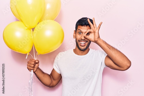 Young latin man holding balloons smiling happy doing ok sign with hand on eye looking through fingers © Krakenimages.com