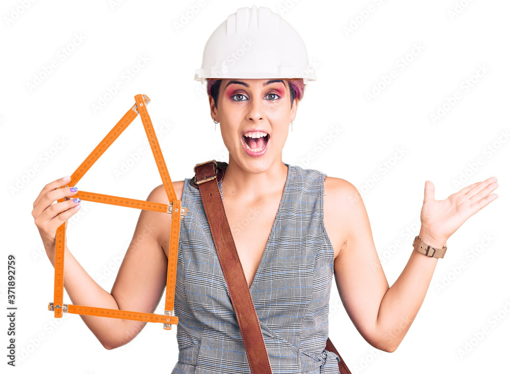 Young beautiful woman wearing architect hardhat holding build project celebrating victory with happy smile and winner expression with raised hands Young beautiful woman wearing architect hardhat holding build project celebrating victory with happy smile and winner expression with raised hands