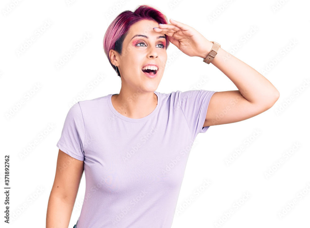 Young beautiful woman with pink hair wearing casual clothes very happy and smiling looking far away with hand over head. searching concept. Young beautiful woman with pink hair wearing casual clothes very happy and smiling looking far away with hand over head. searching concept.