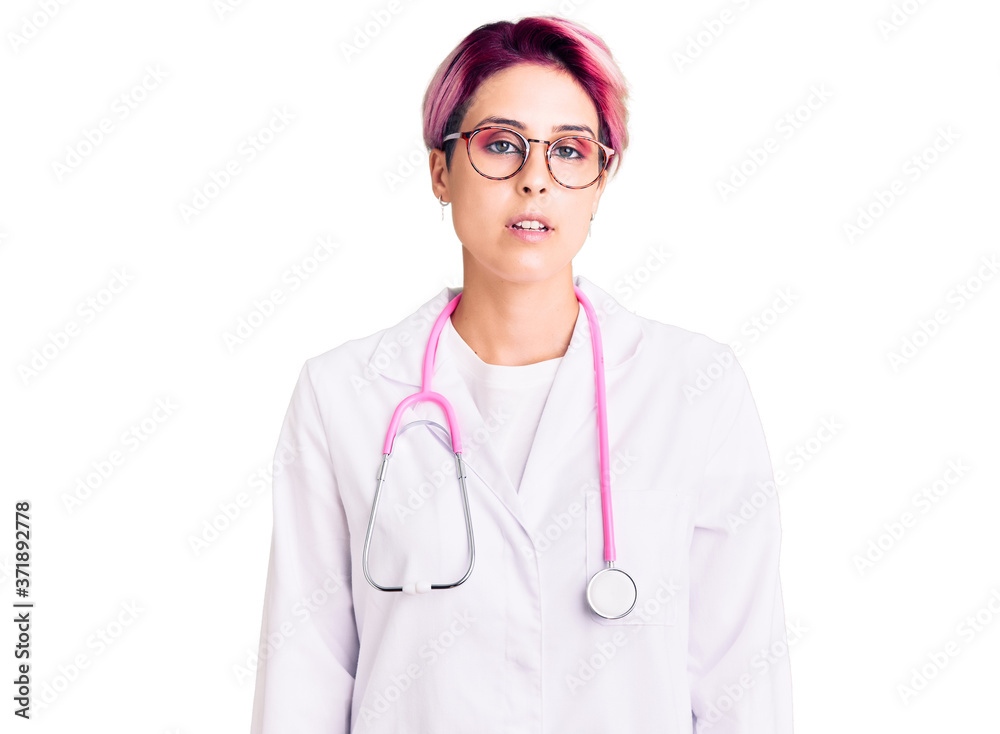 Young beautiful woman with pink hair wearing doctor uniform relaxed with serious expression on face. simple and natural looking at the camera. Young beautiful woman with pink hair wearing doctor uniform relaxed with serious expression on face. simple and natural looking at the camera.