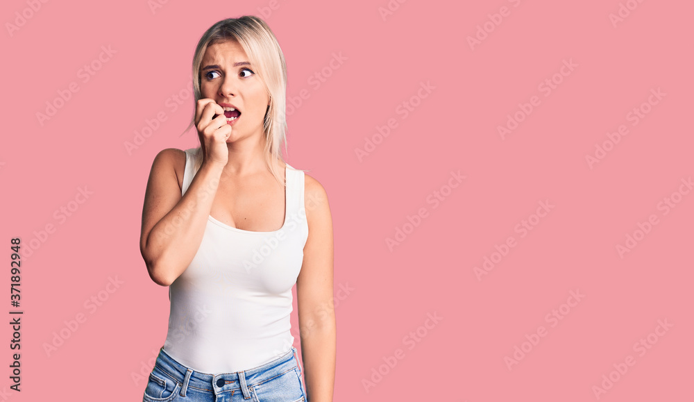 Young beautiful blonde woman wearing casual sleeveless t-shirt looking stressed and nervous with hands on mouth biting nails. anxiety problem. Young beautiful blonde woman wearing casual sleeveless t-shirt looking stressed and nervous with hands on mouth biting nails. anxiety problem.