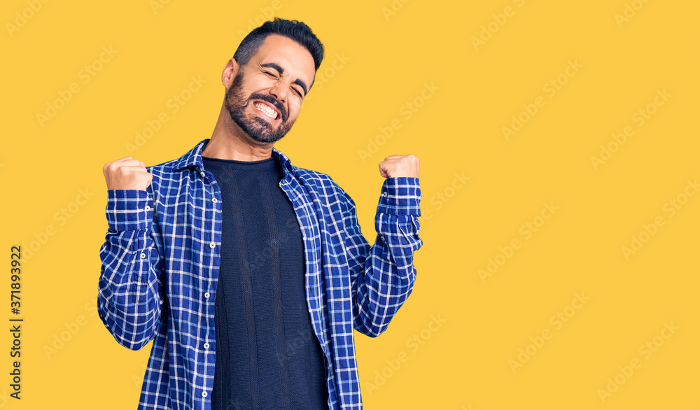 Young hispanic man wearing casual clothes very happy and excited doing winner gesture with arms raised, smiling and screaming for success. celebration concept. Young hispanic man wearing casual clothes very happy and excited doing winner gesture with arms raised, smiling and screaming for success. celebration concept.