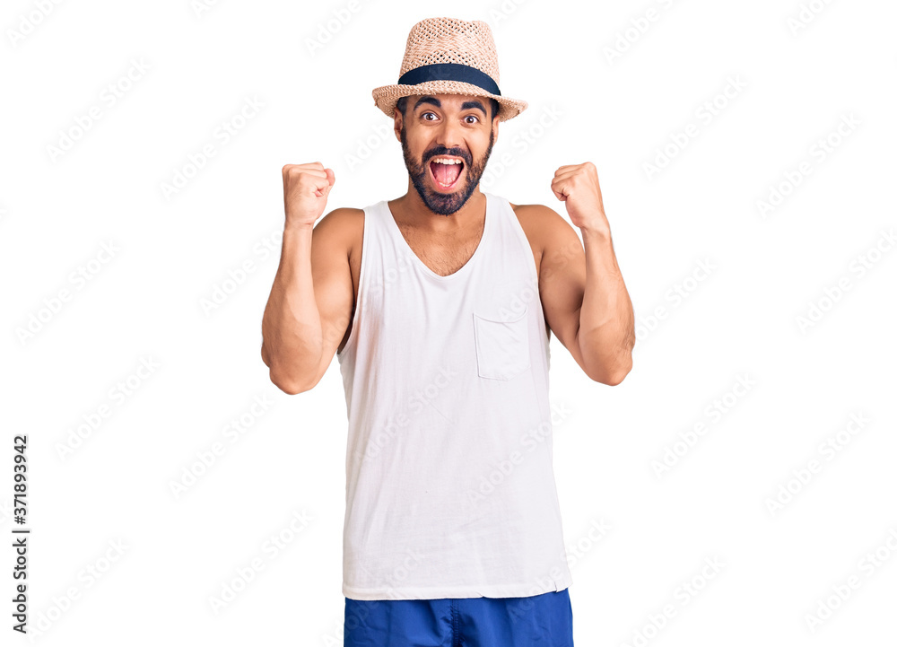 Naklejka premium Young hispanic man wearing casual summer hat celebrating surprised and amazed for success with arms raised and open eyes. winner concept.