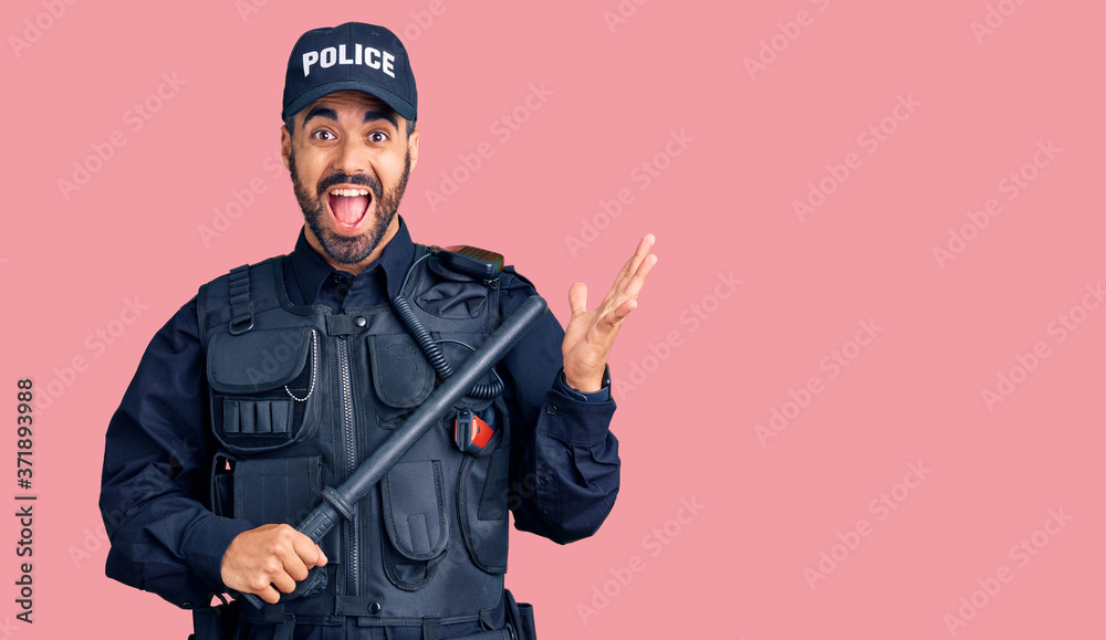 Young hispanic man wearing police uniform holding baton celebrating victory with happy smile and winner expression with raised hands Young hispanic man wearing police uniform holding baton celebrating victory with happy smile and winner expression with raised hands