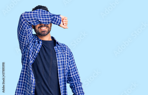 Young hispanic man wearing casual clothes covering eyes with arm smiling cheerful and funny. blind concept.