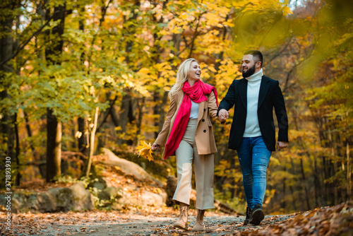 Young couple in love holding hands and walking through a park on a sunny autumn day. Lovers walking hand in hand. Autumnal weather. Romantic and love.