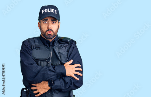 Young hispanic man wearing police uniform shaking and freezing for winter cold with sad and shock expression on face