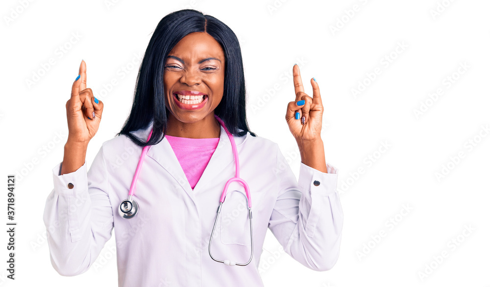 Young african american woman wearing doctor stethoscope shouting with crazy expression doing rock symbol with hands up. music star. heavy music concept. Young african american woman wearing doctor stethoscope shouting with crazy expression doing rock symbol with hands up. music star. heavy music concept.