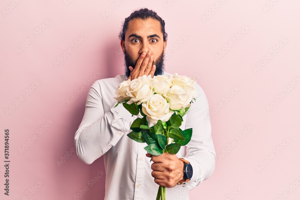 Young arab man holding flowers covering mouth with hand, shocked and afraid for mistake. surprised expression Young arab man holding flowers covering mouth with hand, shocked and afraid for mistake. surprised expression