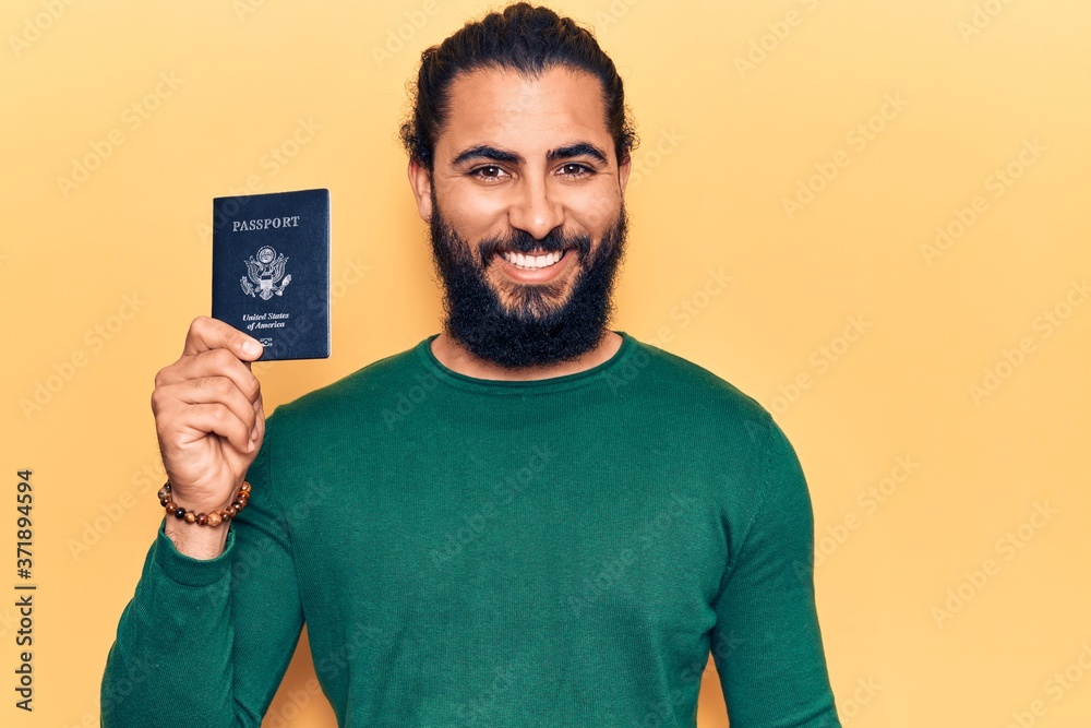 Young arab man holding united states passport looking positive and happy standing and smiling with a confident smile showing teeth