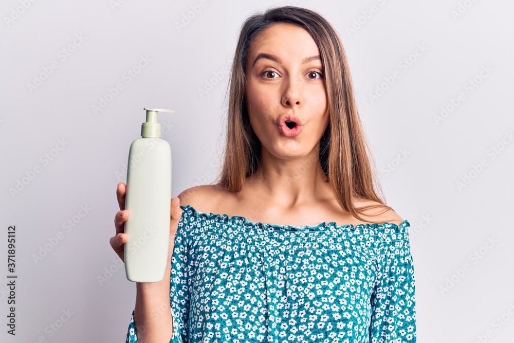 Young beautiful girl holding bottle of cream lotion scared and amazed with open mouth for surprise, disbelief face Young beautiful girl holding bottle of cream lotion scared and amazed with open mouth for surprise, disbelief face