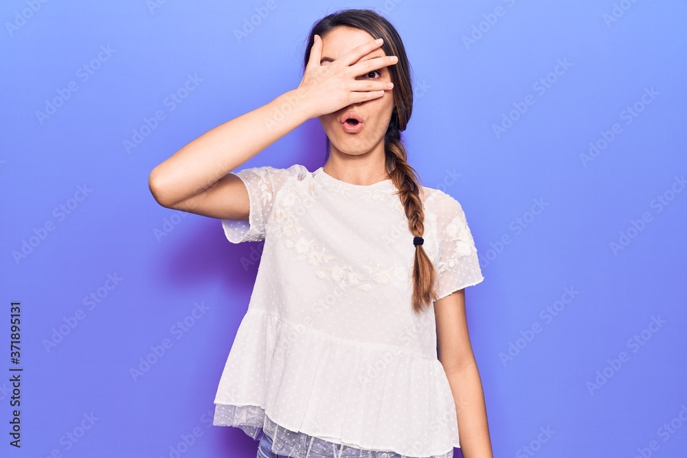 Young beautiful girl wearing casual t-shirt peeking in shock covering face and eyes with hand, looking through fingers afraid Young beautiful girl wearing casual t-shirt peeking in shock covering face and eyes with hand, looking through fingers afraid