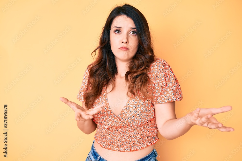 Young beautiful brunette woman wearing casual summer clothes clueless and confused expression with arms and hands raised. doubt concept. Young beautiful brunette woman wearing casual summer clothes clueless and confused expression with arms and hands raised. doubt concept.