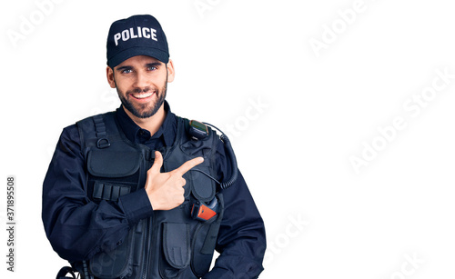 Young handsome man with beard wearing police uniform cheerful with a smile of face pointing with hand and finger up to the side with happy and natural expression on face