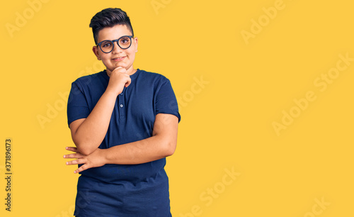 Little boy kid wearing casual clothes and glasses looking confident at the camera with smile with crossed arms and hand raised on chin. thinking positive.