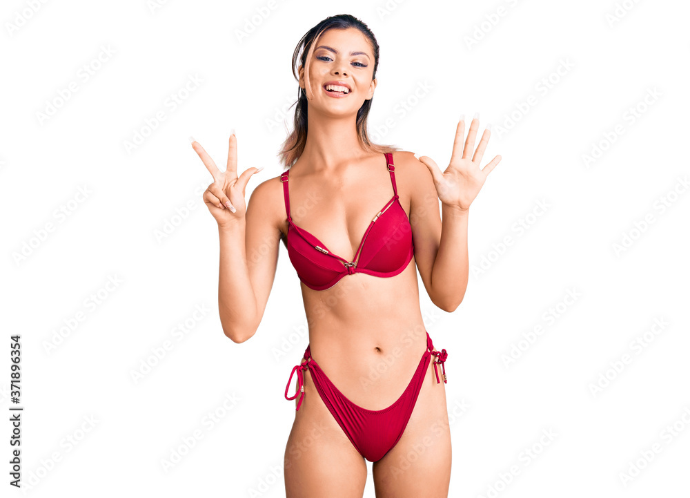 Young beautiful woman wearing bikini showing and pointing up with fingers number eight while smiling confident and happy. Young beautiful woman wearing bikini showing and pointing up with fingers number eight while smiling confident and happy.
