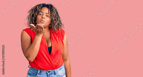 Young african american plus size woman wearing casual style with sleeveless shirt looking at the camera blowing a kiss with hand on air being lovely and sexy. love expression.
