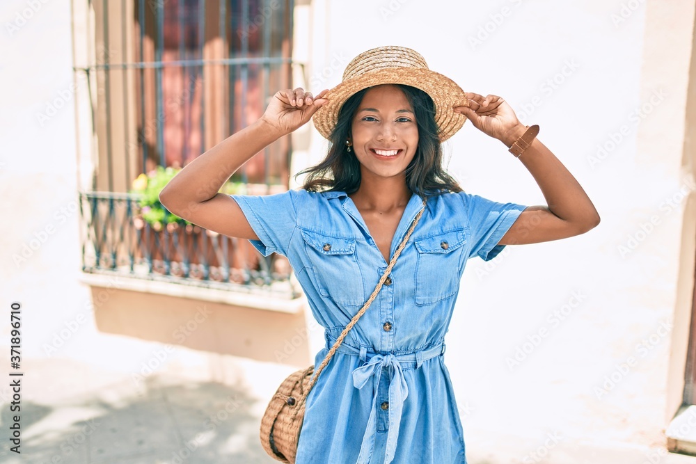 Young beautiful indian woman wearing summer hat smiling happy walking at the city.